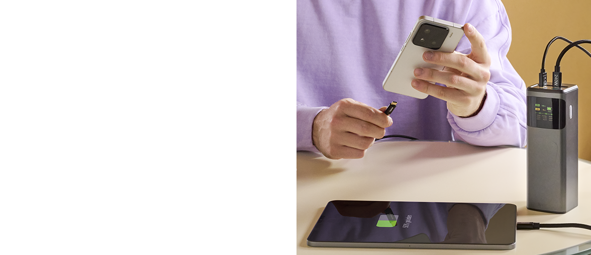 A man connects his smartphone via USB cable to the Hama Powerpack, which is already charging a tablet.
